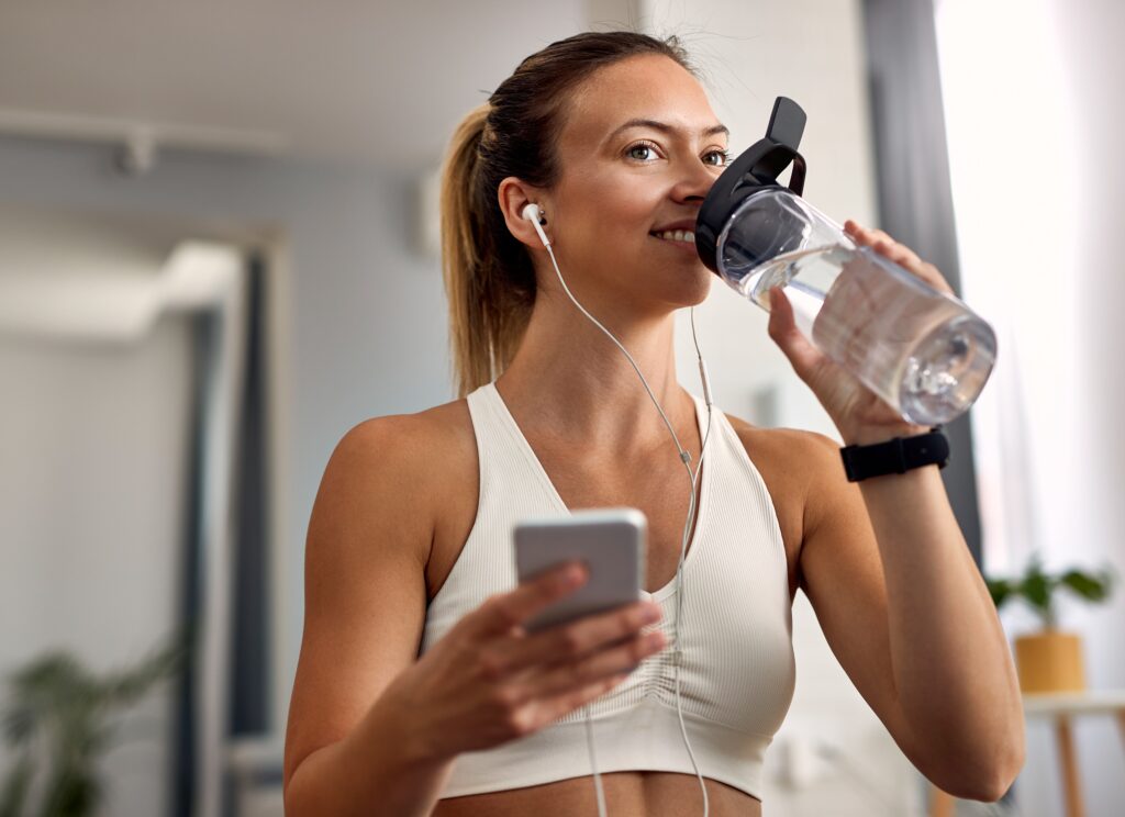 happy athletic woman drinking water after exercising at home.