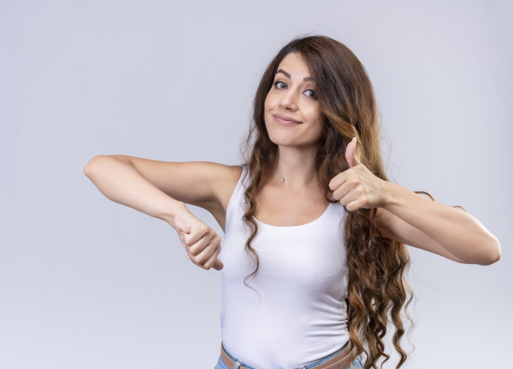 pleased young beautiful girl showing thumbs up and down on isolated white background