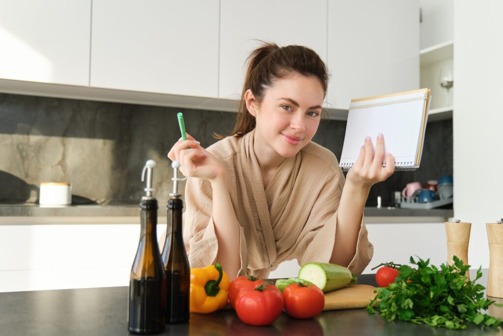 portrait of woman cooking in the kitchen, reading her notes, checking recipe while preparing meal, making breakfast salad, writing down grocery list