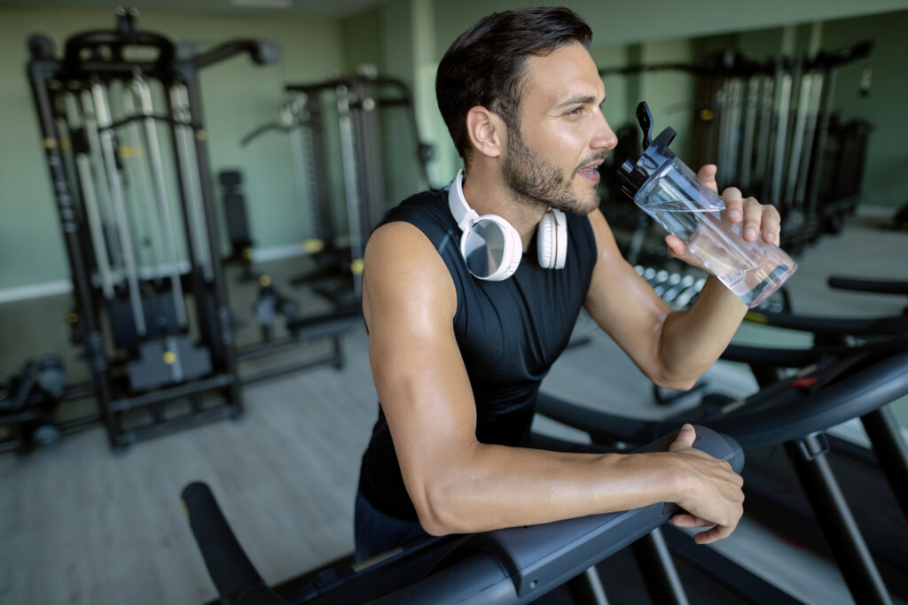 thirsty athlete drinking water after running on treadmill at hea