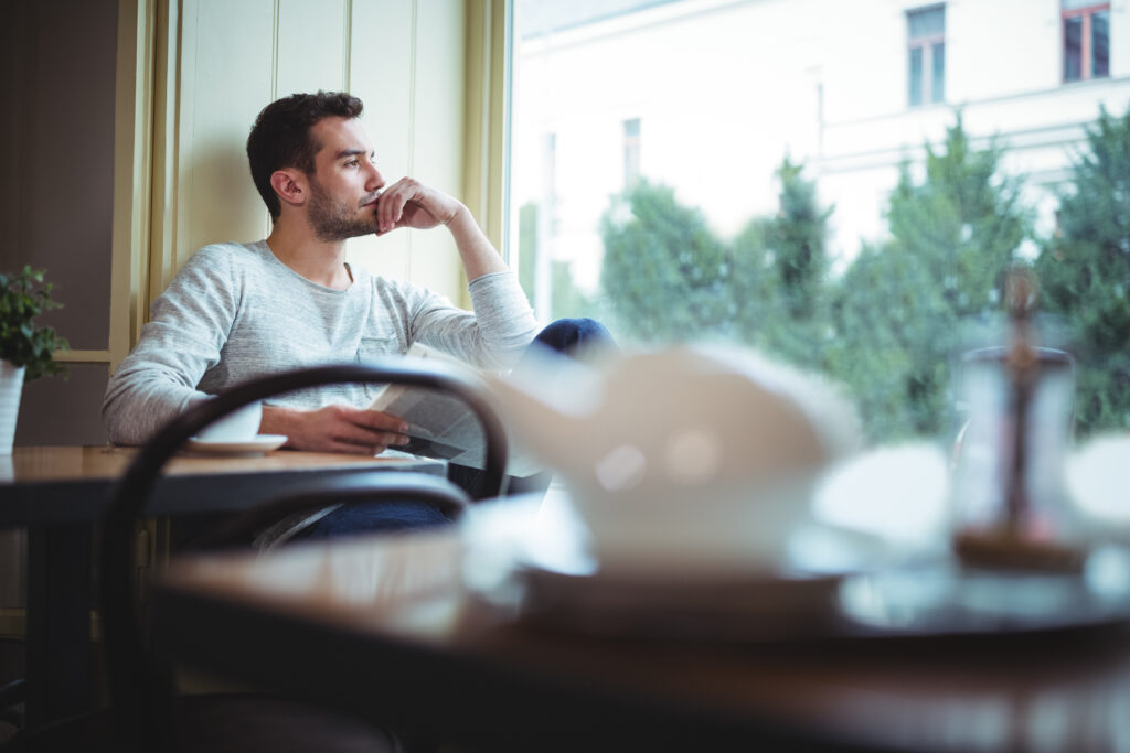 thoughtful man looking through window while reading newspaper
